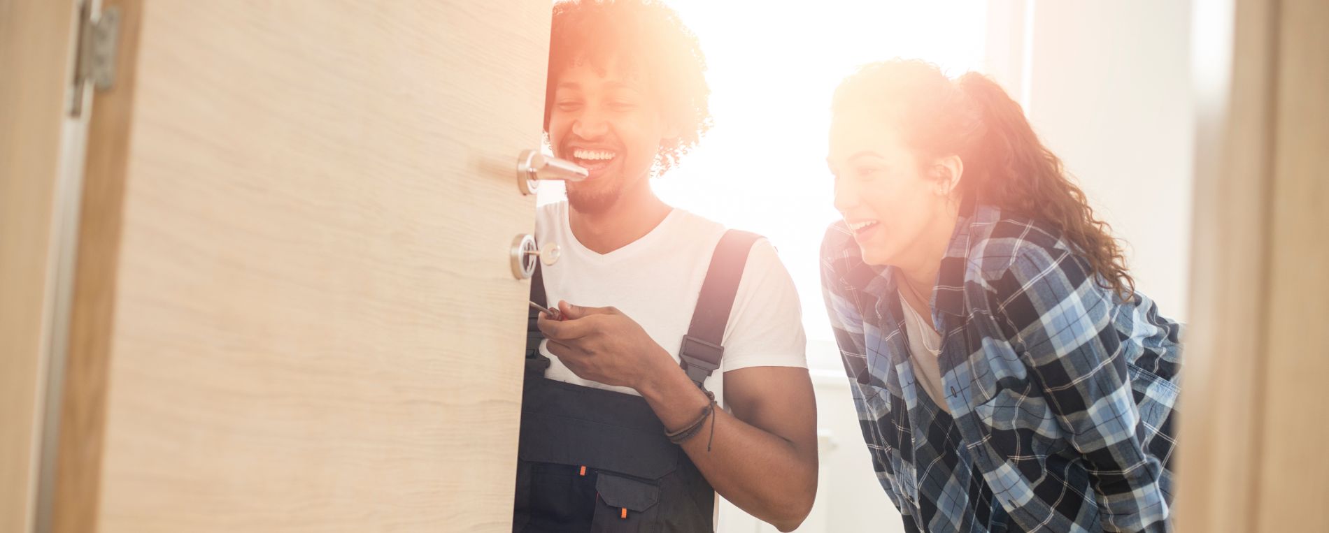 A female stands by locksmith worker who is mending a lock